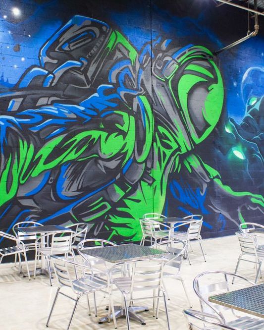 Green and blue graffiti astronaut painted along a cinder block wall above cafe seating
