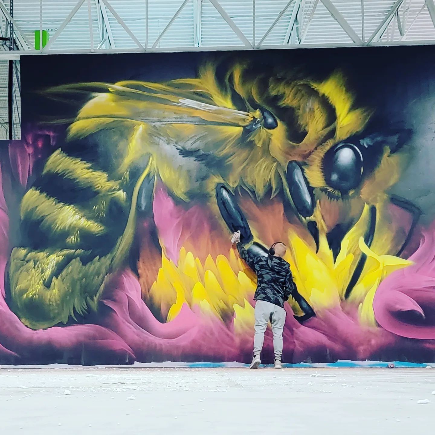 SRIL ART freehand-painting a large-scale bee mural, dwarfed by the finished wall