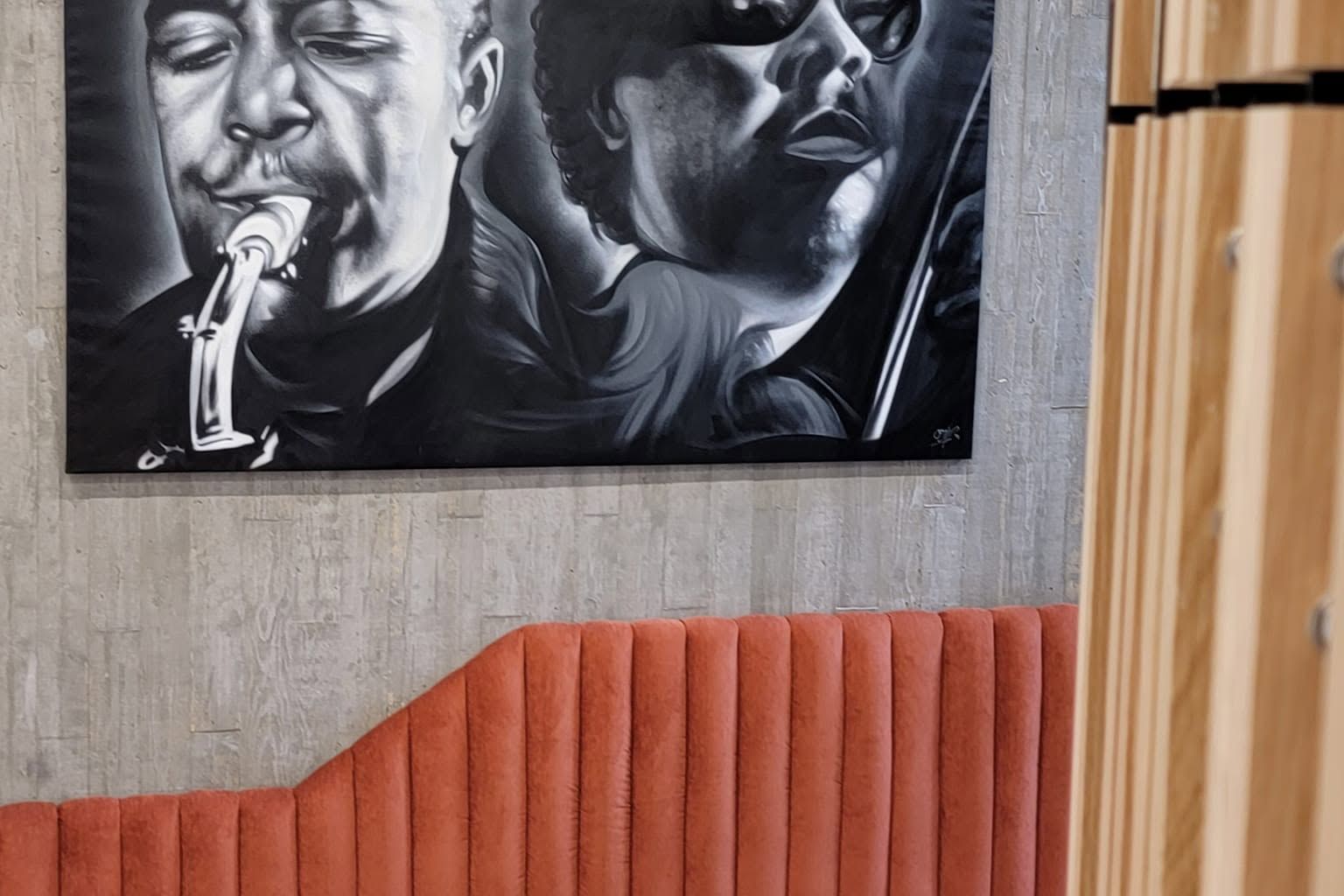 Large black-and-white aerosol canvas of two musicians, hung above a rust-colored banquette