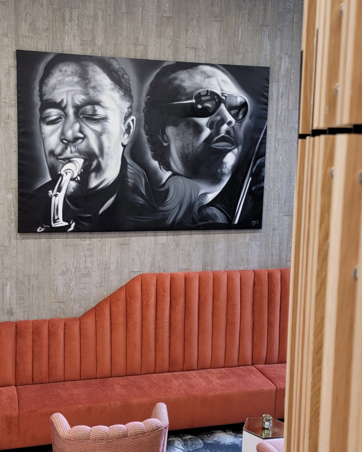 Large black-and-white aerosol canvas of a saxophonist and a singer, hung above a rust-colored banquette