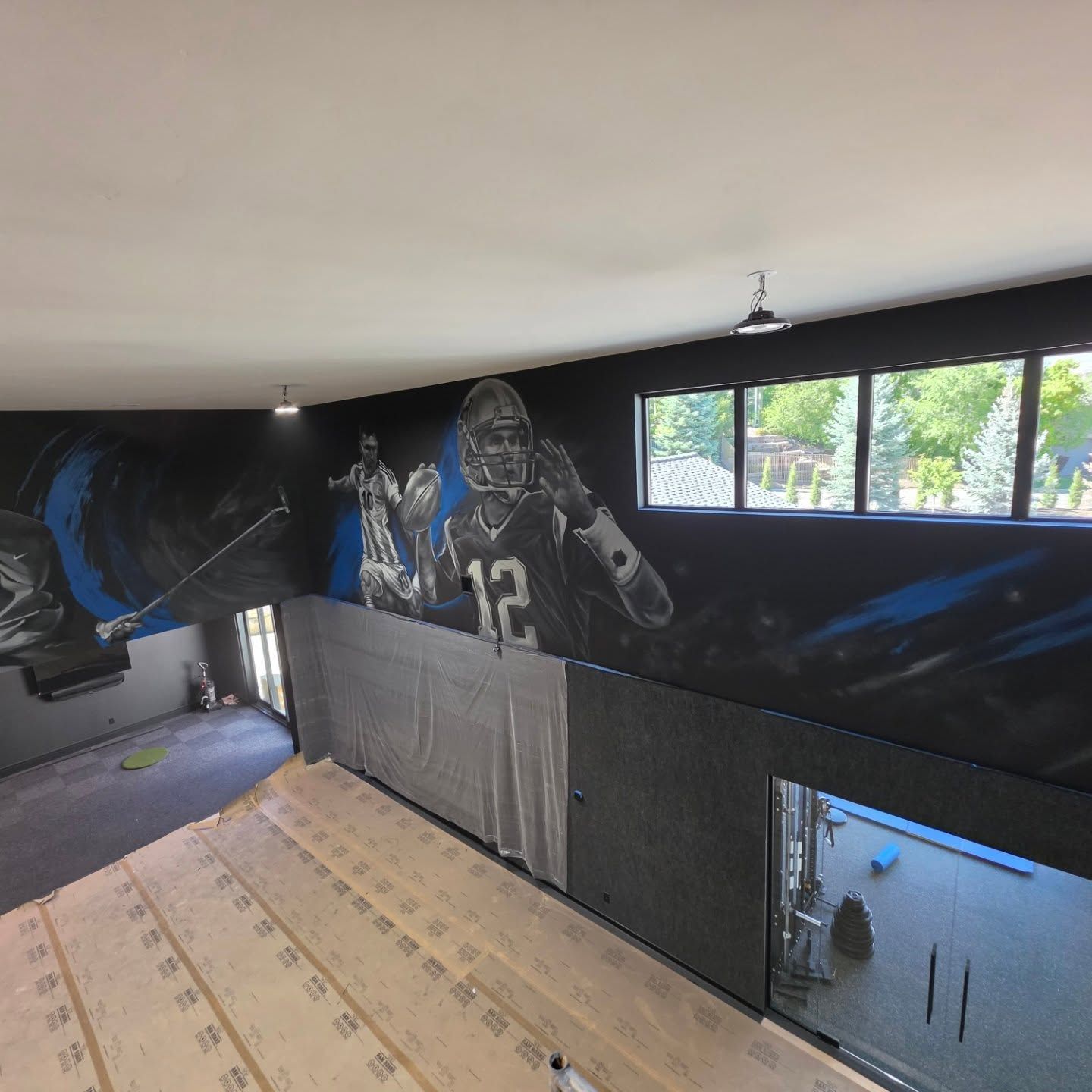Charcoal court wall wrapping a corner, painted athletes above the padding, gym visible through glass