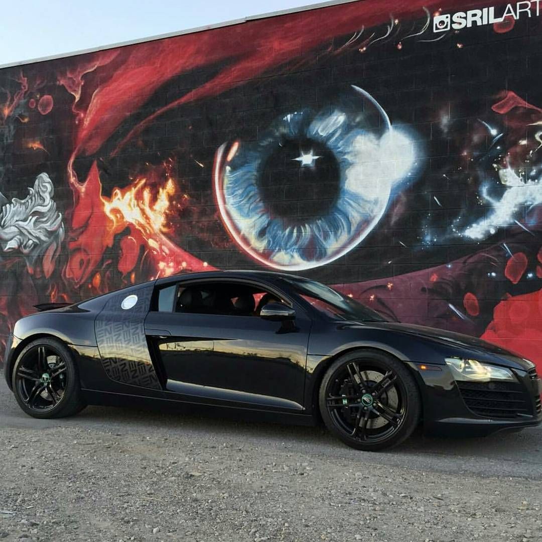 Giant eye with a star in the pupil, painted in reds, with a black sports car parked beneath it