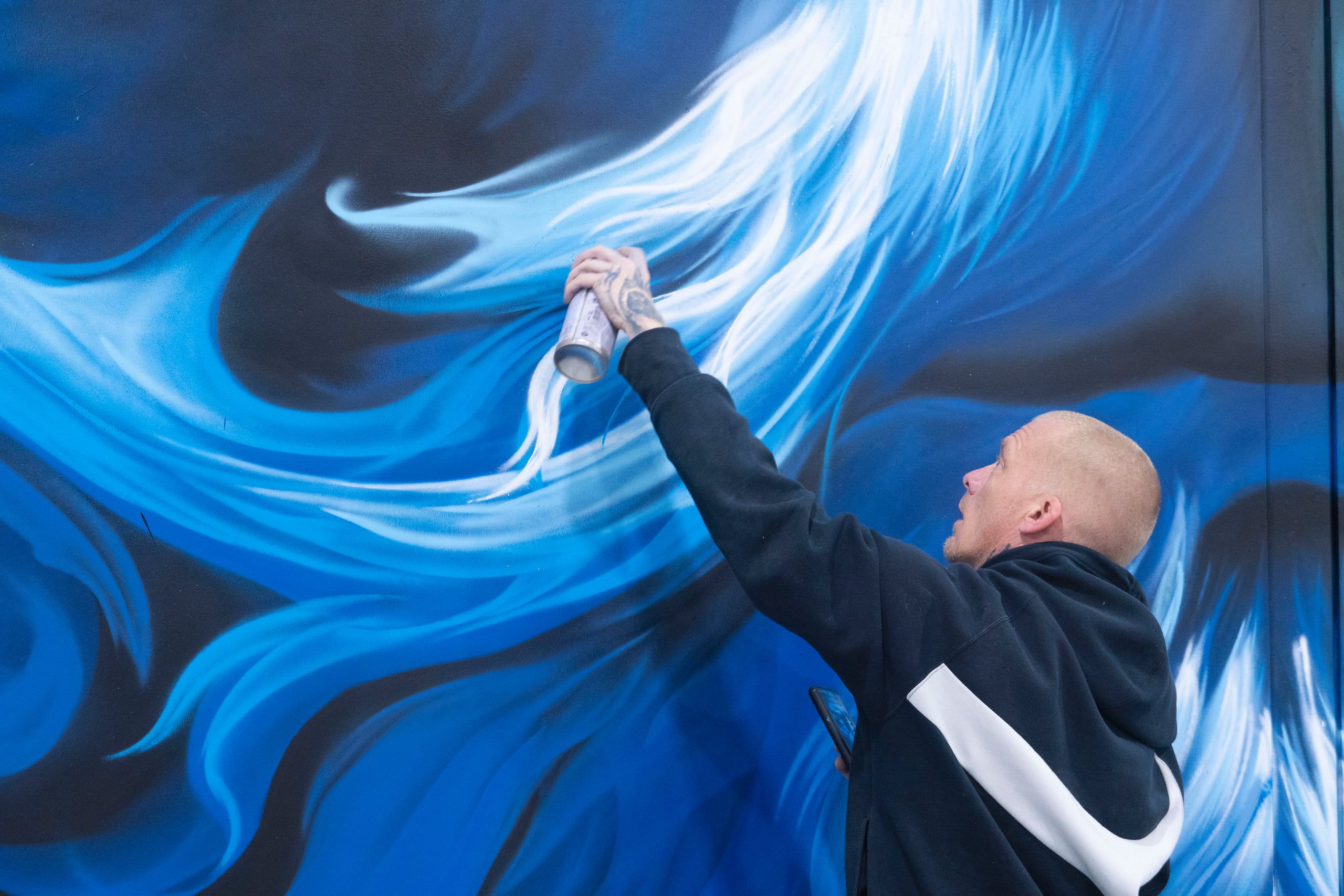 SRIL ART spray-painting a blue smoke flourish on the Zeus mural, can raised overhead