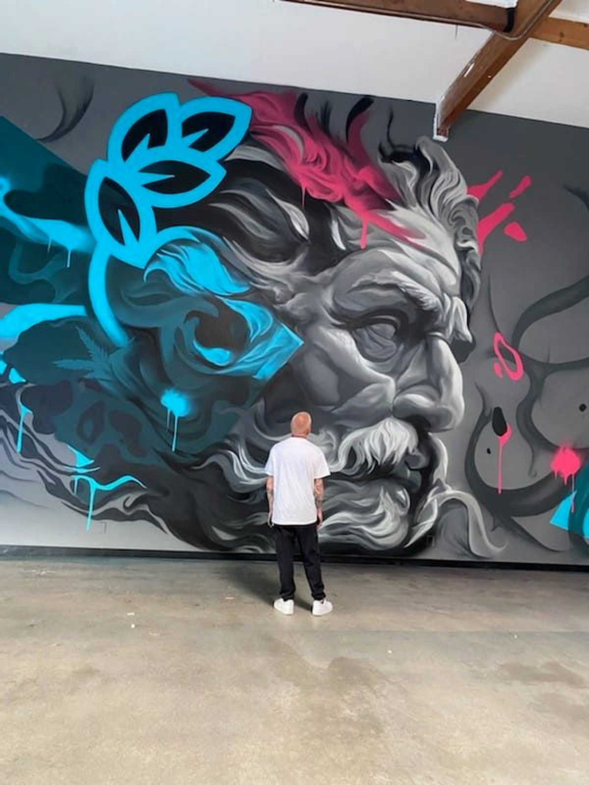 SRIL ART standing in front of the finished grayscale Zeus mural with cyan laurel accents