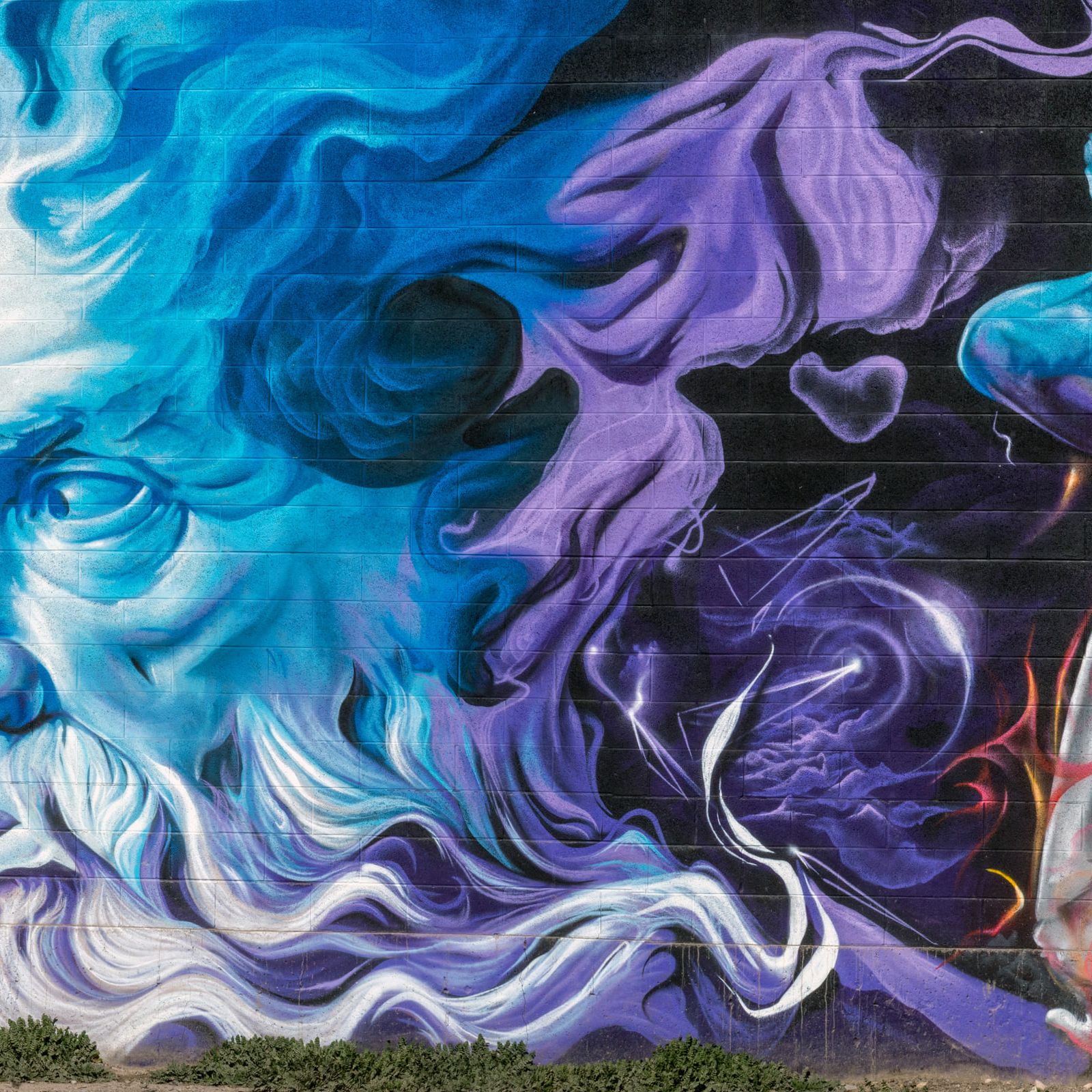 A long cinder-block wall painted end to end: bearded blue god, purple smoke, a falling figure in fire, and a giant eye