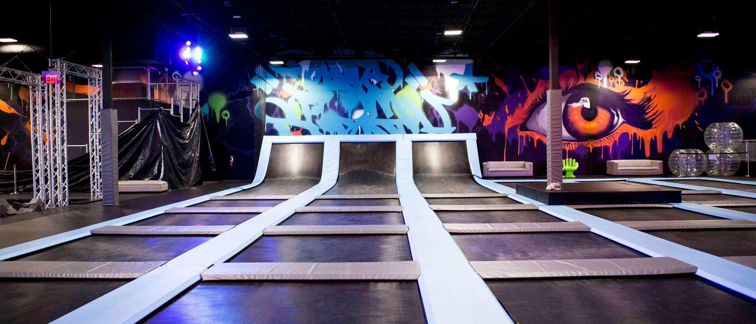 Blue wildstyle lettering and a large orange eye painted across the back walls of a trampoline park