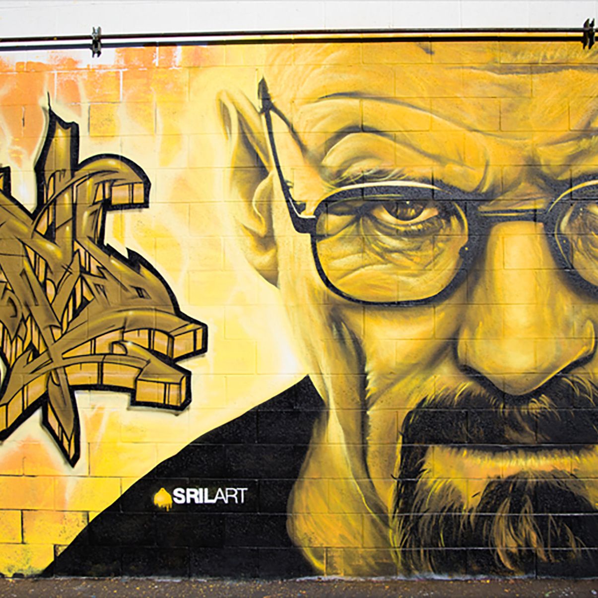 Yellow-toned Walter White portrait beside gold wildstyle graffiti lettering on an exterior cinder block wall