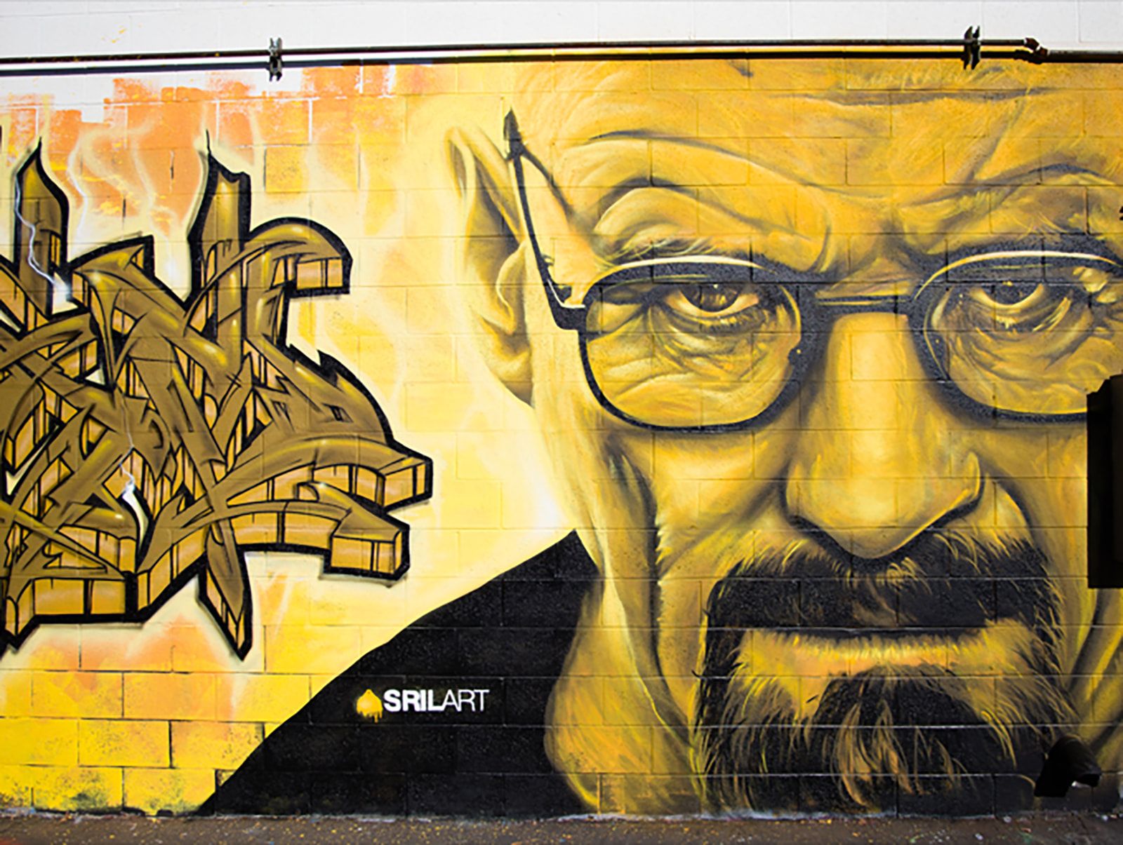 Yellow-toned Walter White portrait beside gold wildstyle graffiti lettering on an exterior cinder block wall