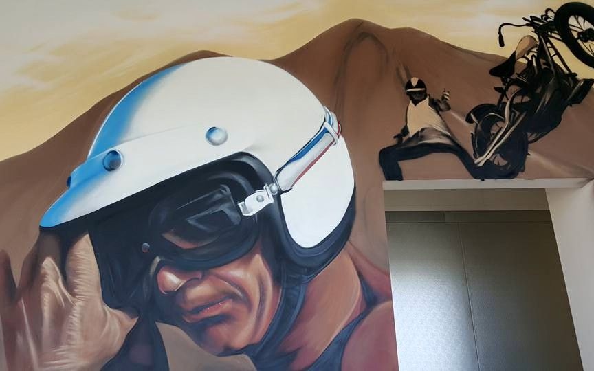 Hand-painted portrait mural of a helmeted motorcycle racer beside a stunt-rider scene on an interior wall