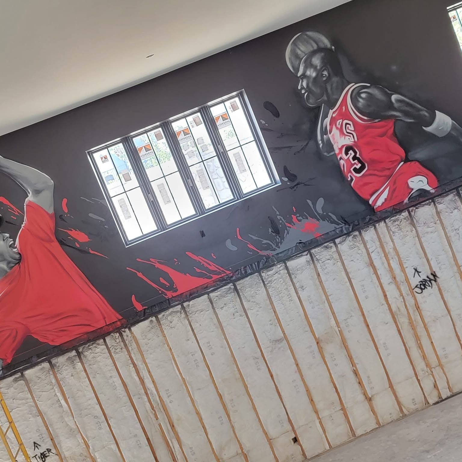 Grayscale basketball players in red jerseys painted along a dark wall above a wooden home court