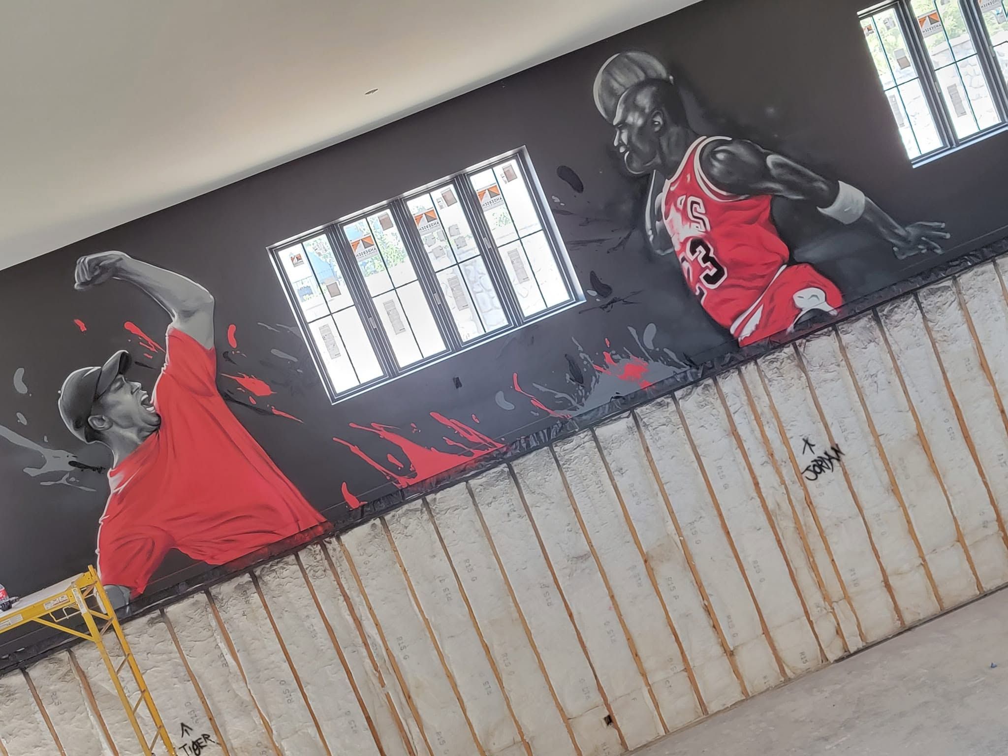 Grayscale basketball players in red jerseys painted along a dark wall above a wooden home court