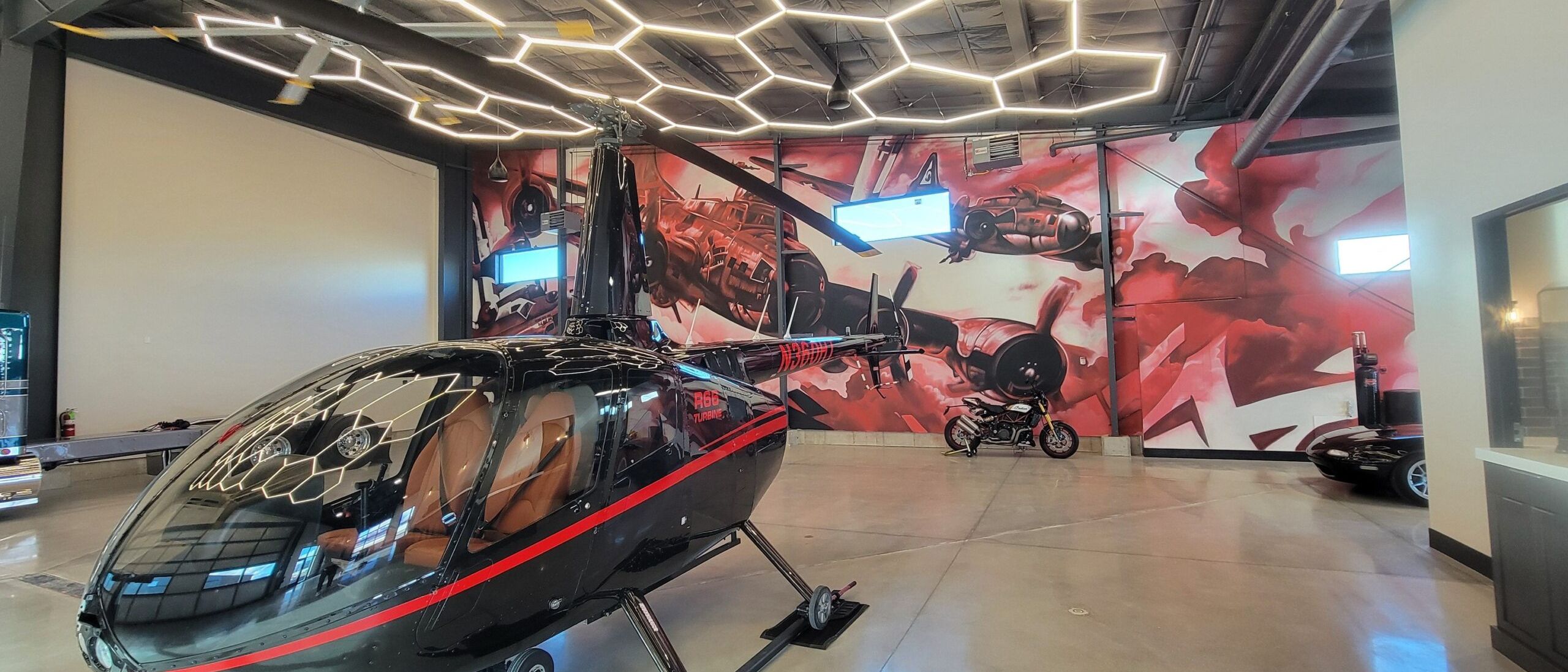 Vintage warplane mural in red and white covering the wall of a private aircraft hangar, helicopter in the foreground