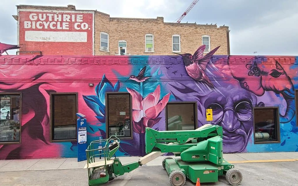 A long brick storefront painted end to end in magenta, purple and teal with hummingbirds and portraits