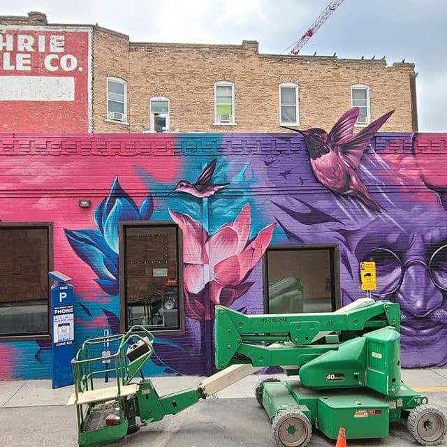 A long brick storefront painted end to end in magenta, purple and teal with hummingbirds and portraits