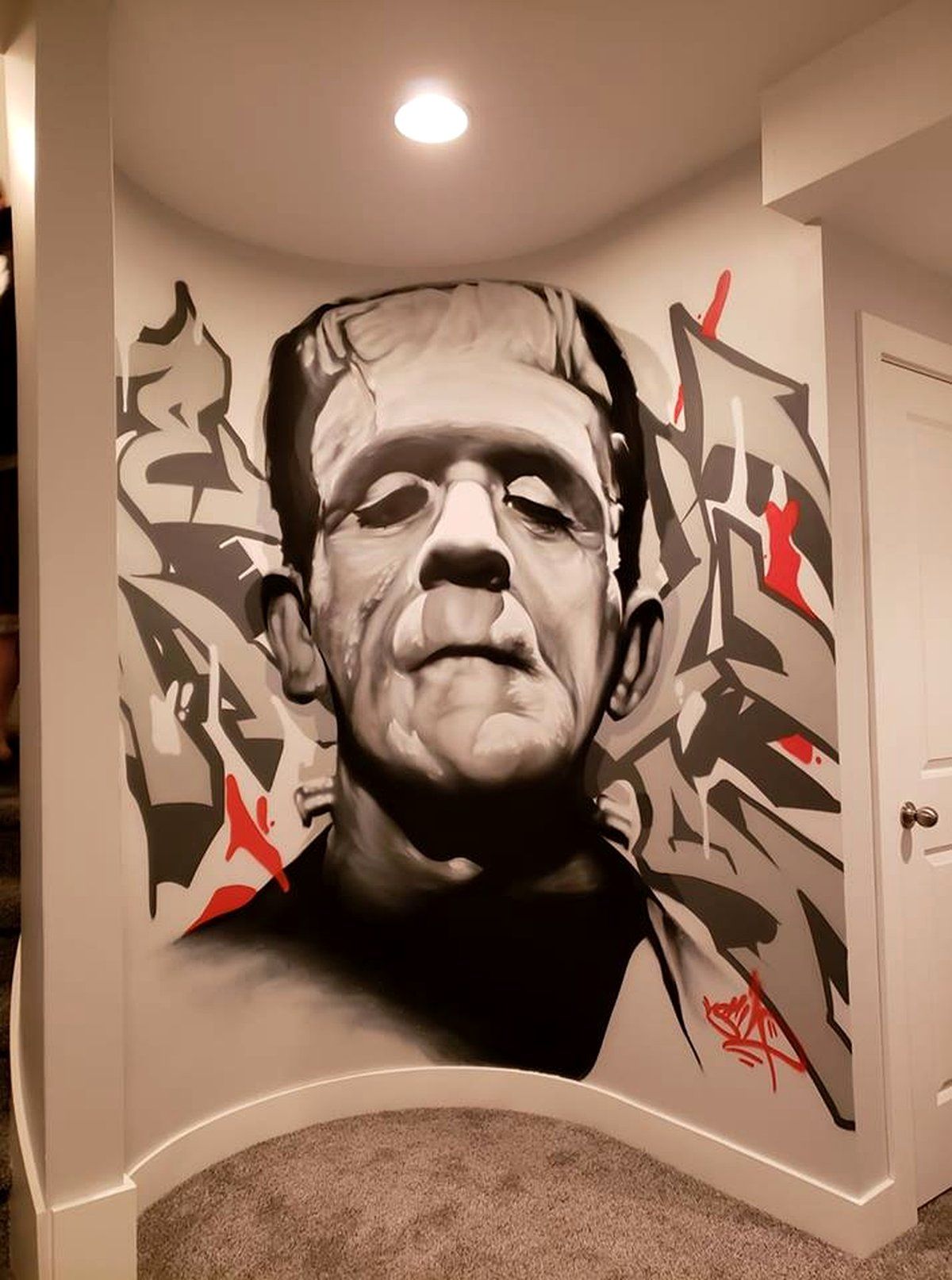 Black and white Frankenstein's monster portrait mural with red graffiti lettering in a hallway