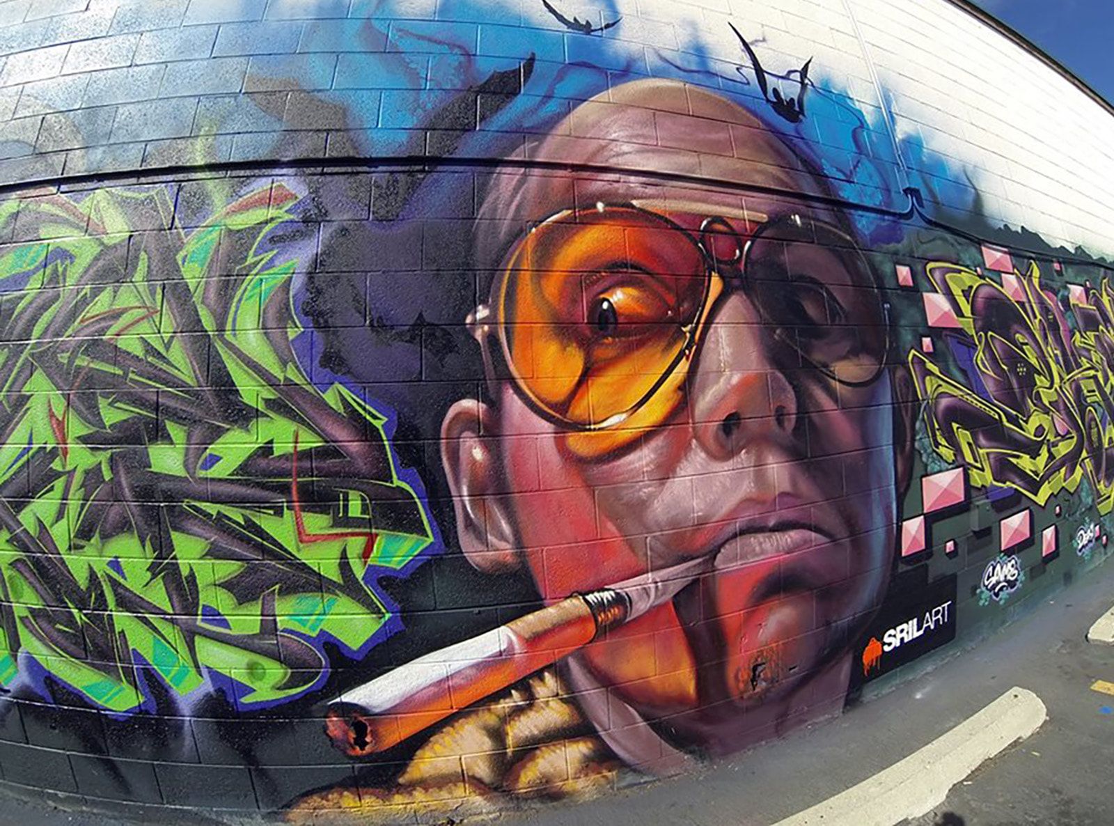Hunter S. Thompson portrait mural with graffiti lettering on an exterior cinder block wall