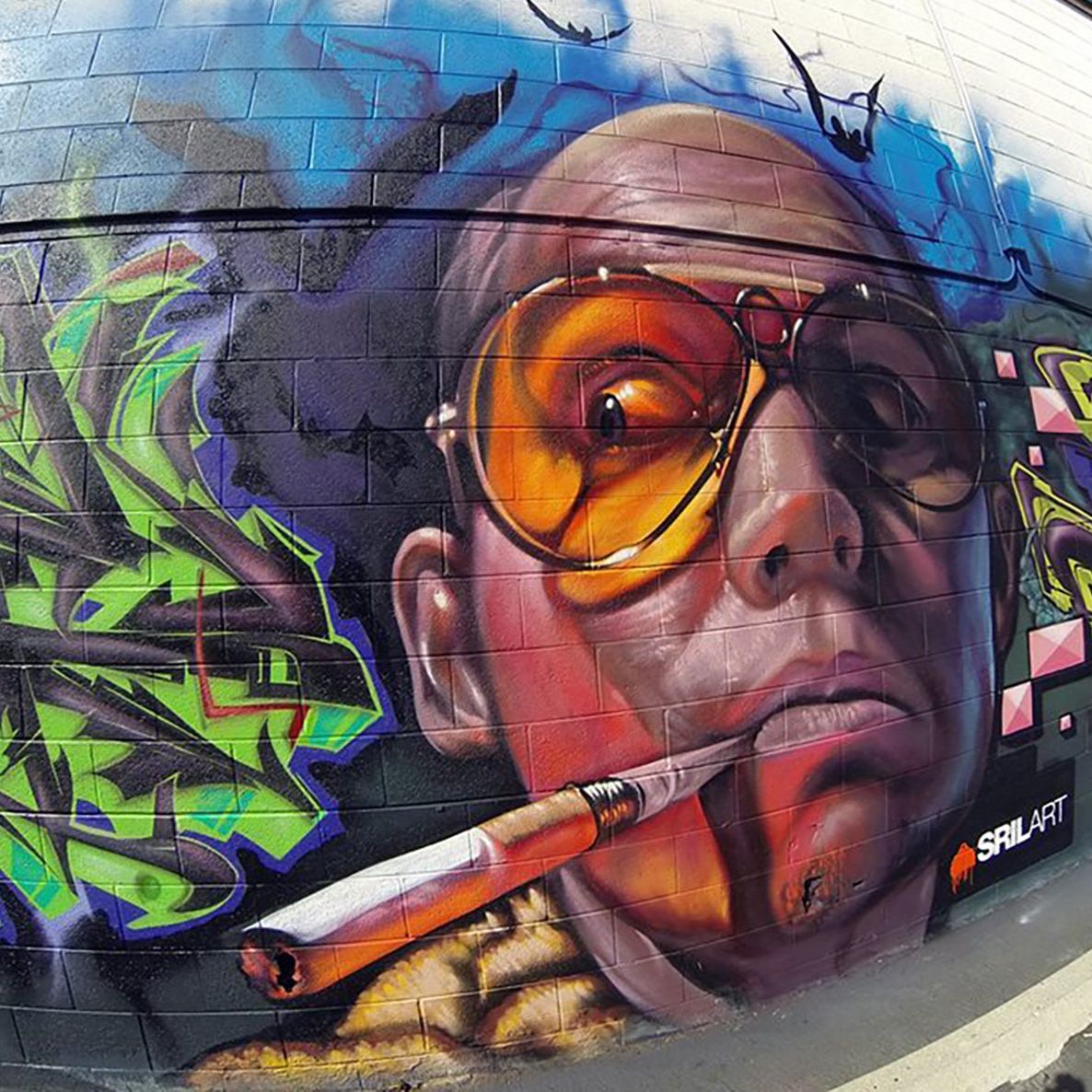 Hunter S. Thompson portrait mural with graffiti lettering on an exterior cinder block wall