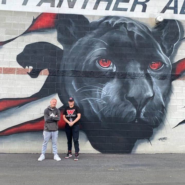 Black panther with red eyes painted on white brick beneath lettering reading Panther Alley