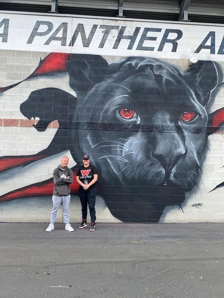 Black panther with red eyes painted on white brick beneath lettering reading Panther Alley