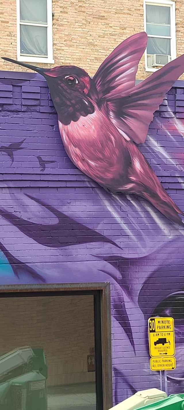 Large magenta hummingbird painted across a purple brick wall above a doorway