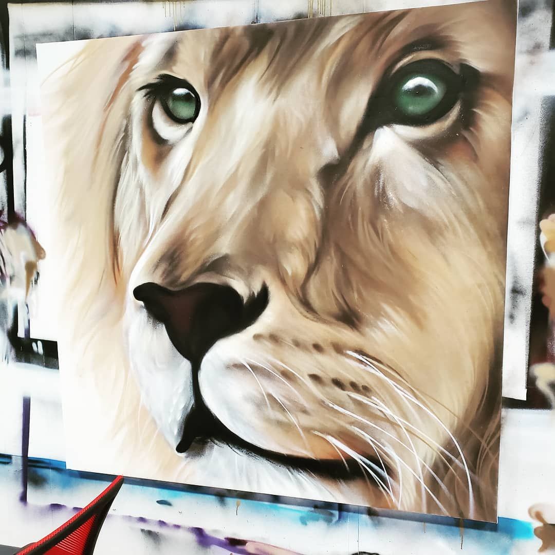 Photorealistic lion portrait painted in aerosol on a large canvas panel in the studio