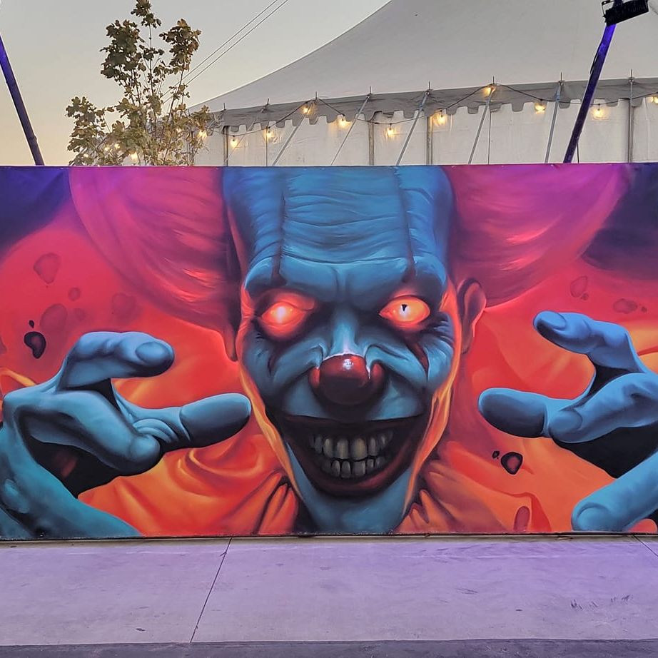 Three blue clowns with glowing eyes across a long panel, lit by festoon lights outside a marquee at dusk