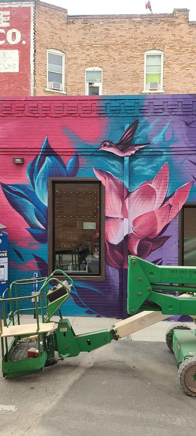 Pink lotus flowers and a hummingbird painted in magenta and blue across brick