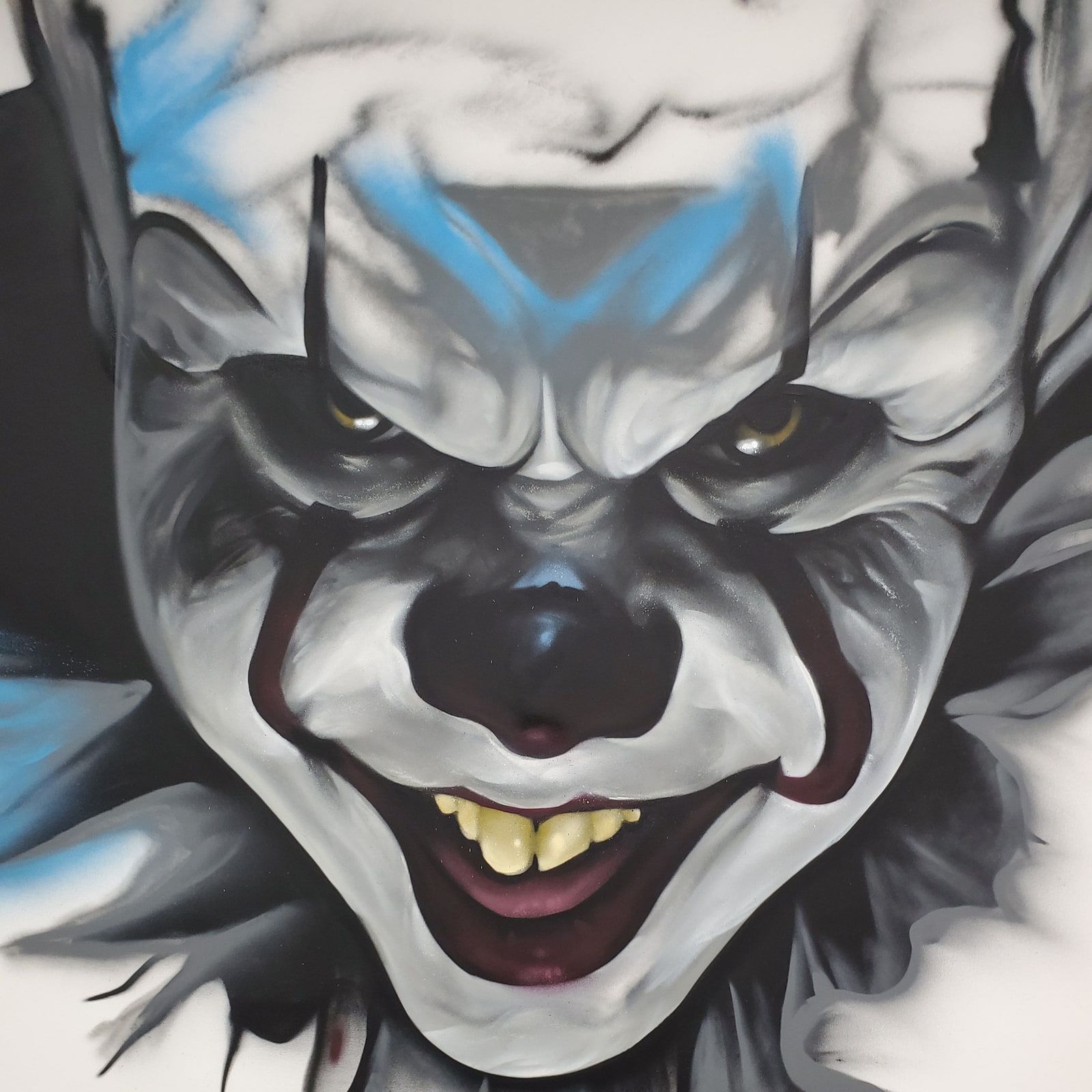 Grinning clown with a red-lined mouth and blue markings above the brow, painted in aerosol on canvas