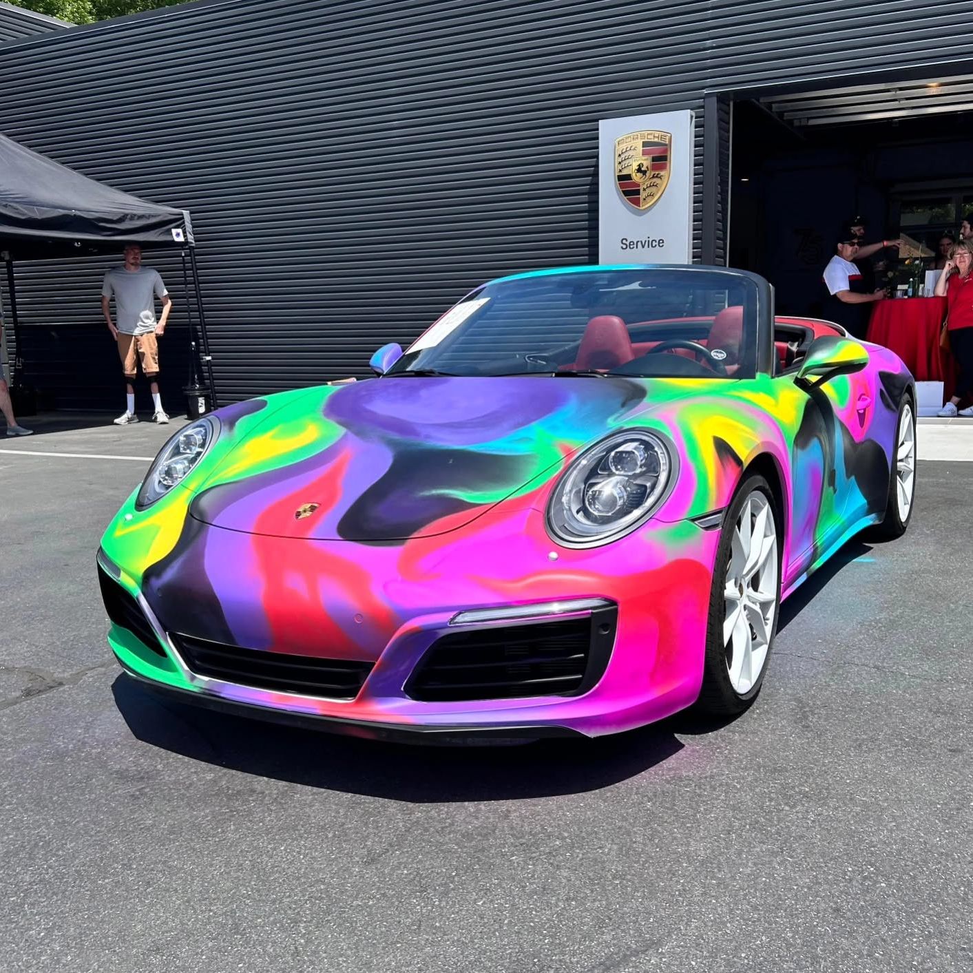 The painted 911 parked outside a Porsche service building beneath the marque's crest