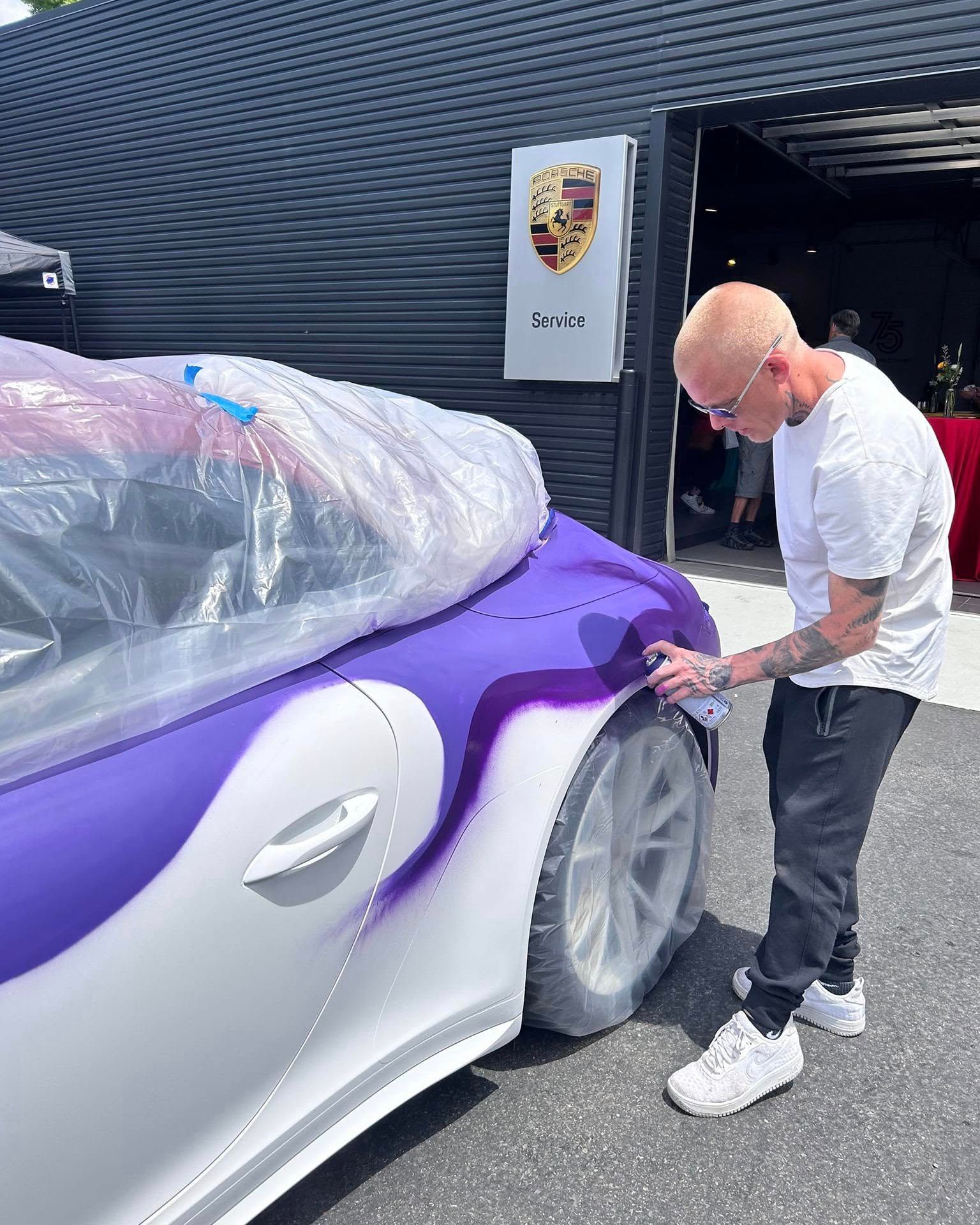 Spraying purple aerosol onto a masked Porsche 911 outside a Porsche service building