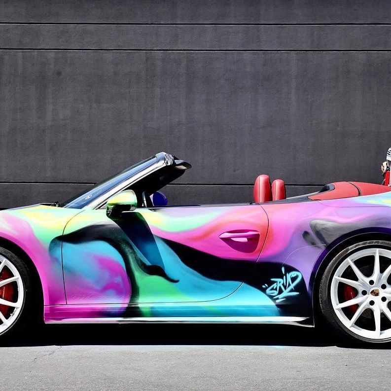 Porsche 911 with the roof down, painted in flowing magenta, green and violet aerosol and signed SRIL behind the door