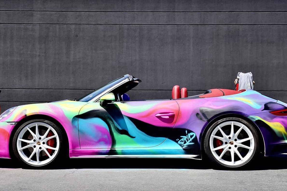 Porsche 911 with the roof down, painted in flowing magenta, green and violet aerosol