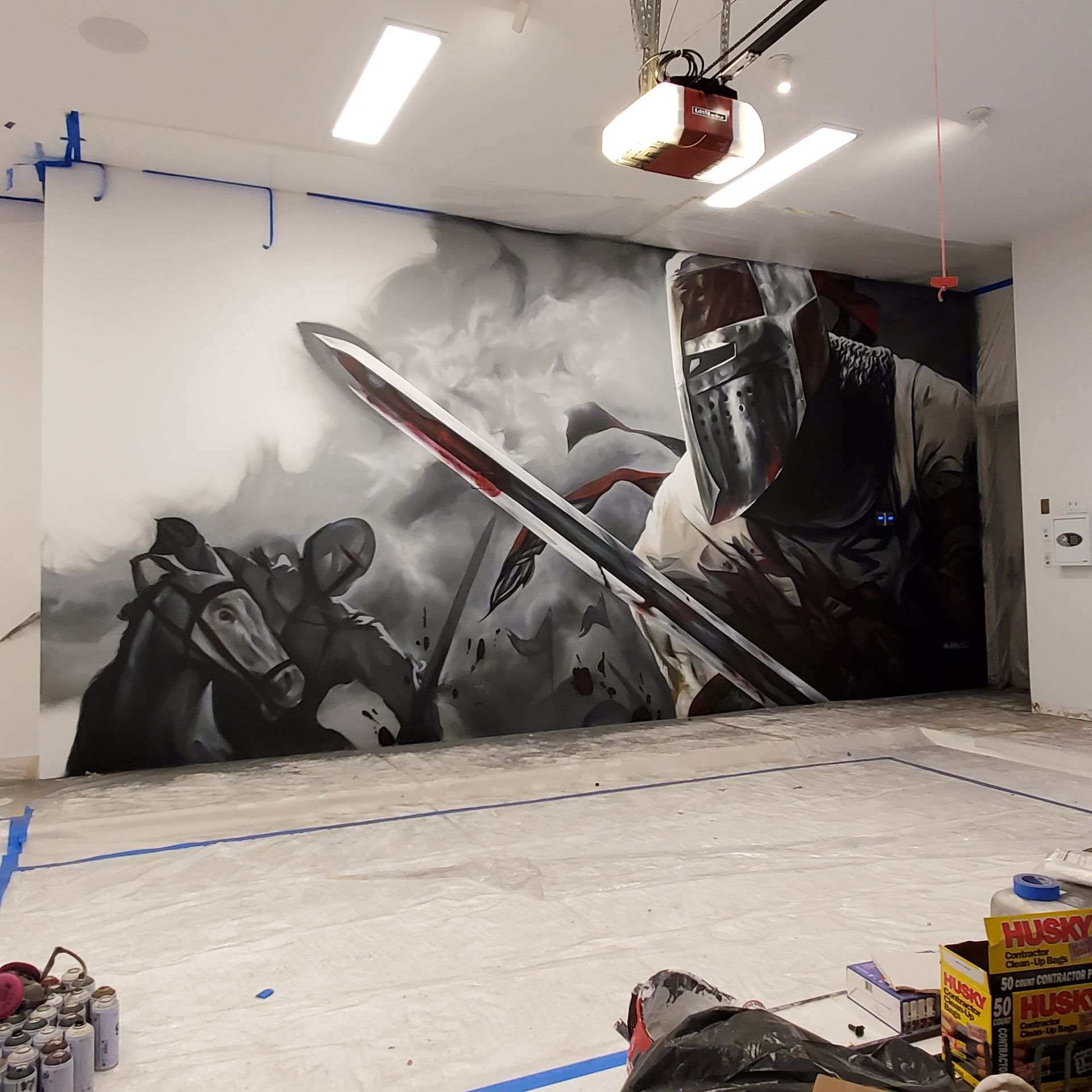 Knight and warhorse taking shape across two walls of a room, spray cans and taped drop cloths on the floor