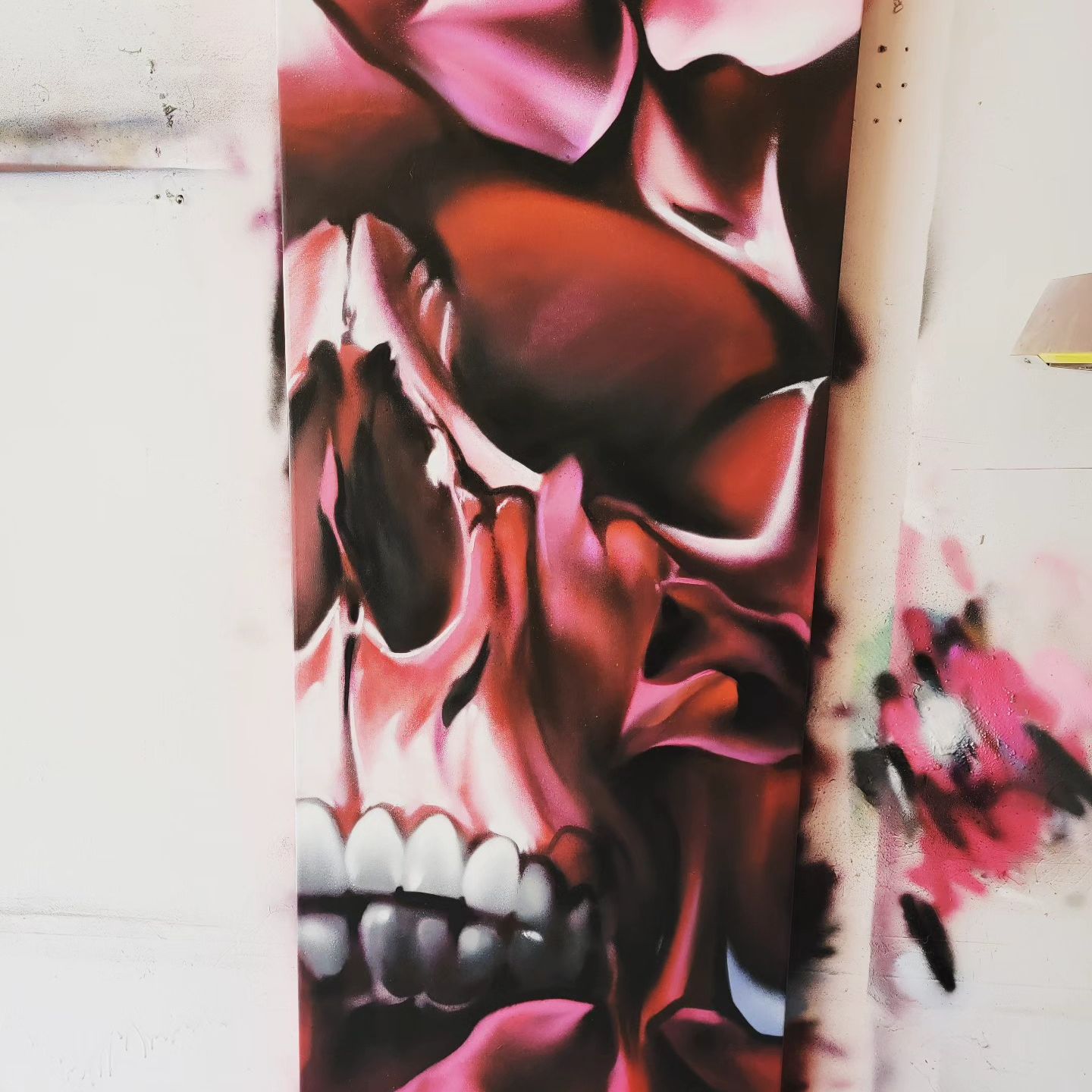 Red and pink aerosol skull painted across a large canvas panel in the studio