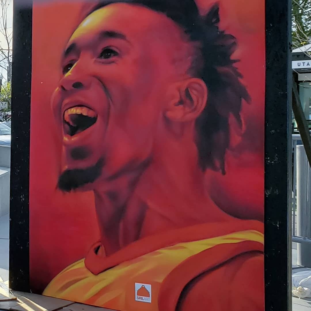 Painted portrait of a Utah Jazz guard mid-celebration in reds and golds, on a framed panel outside the arena