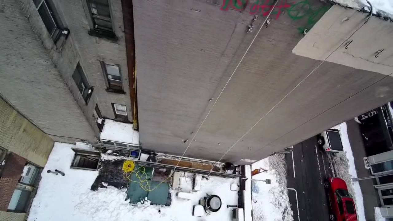 Looking straight down the face of the wall from the roofline, snow on the setbacks and cars below
